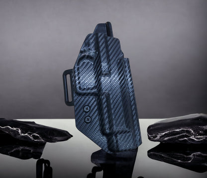A black OWB tactical holster made from Kydex, displayed on a stand against a dark background.